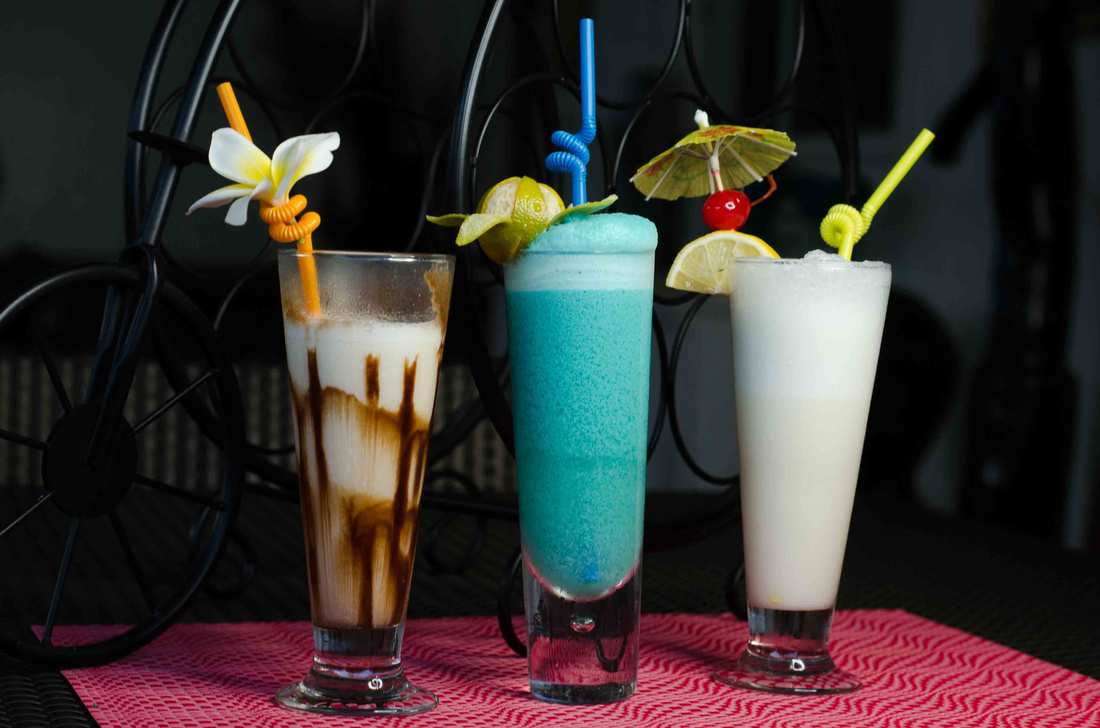 Three tropical cocktails garnished with flowers and fruit